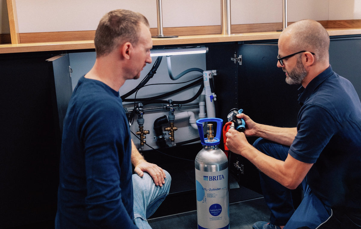 Two men working in a basecabinet with a BRITA CO₂ cylinder installation.