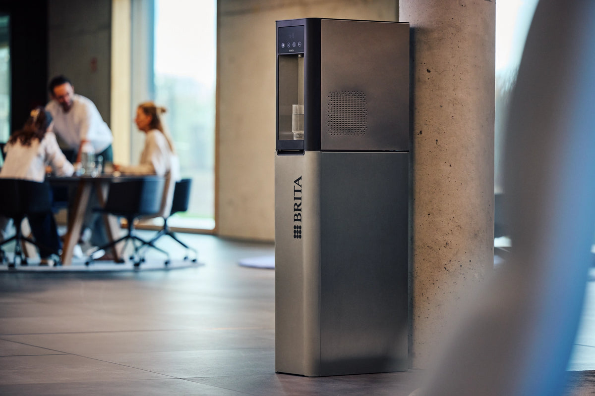 BRITA Top Pro water dispenser in a modern office setting with people at a table in the background.