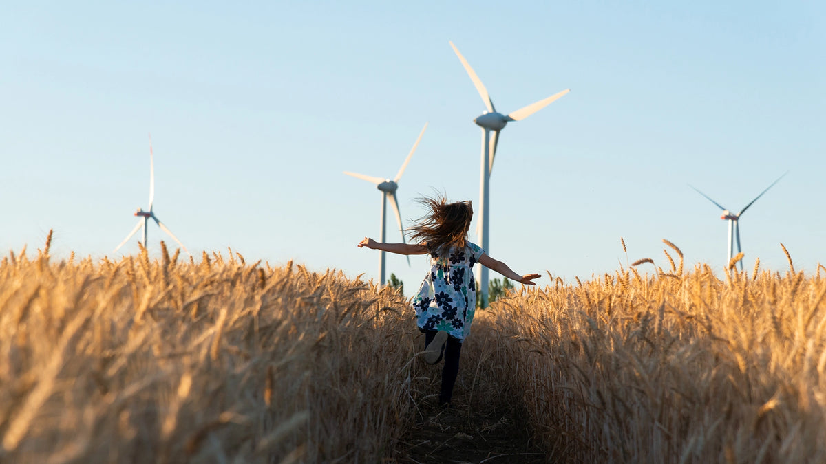 Woman running through a field of tall grass with wind turbines in the background