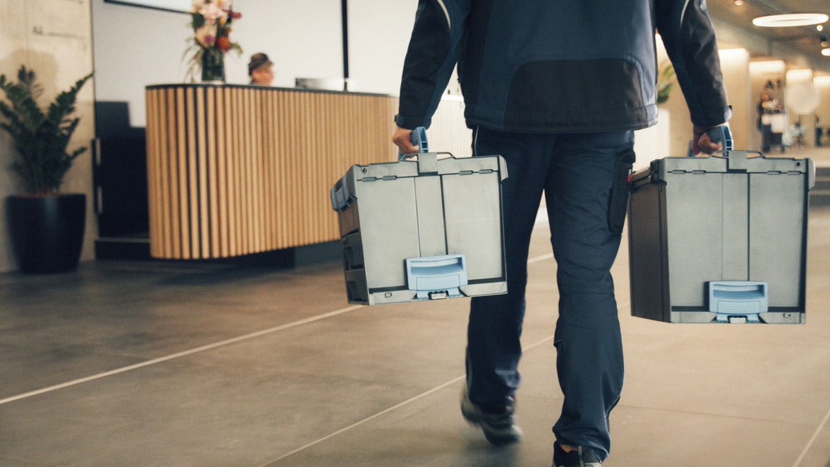 Person walking with two large toolboxes in an entrance hall.
