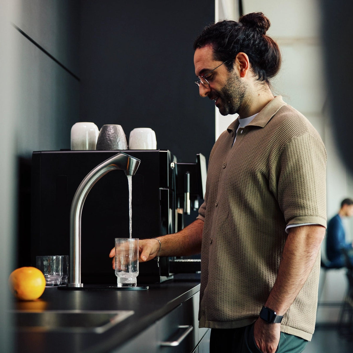A man in an office kitchen dispensing water from a BRITA C-Tap into a glass.